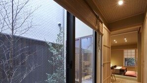 A modern interior with a large sliding glass door leading to a garden, a wooden floor, and a traditional Japanese-style room with tatami mats. - Rinn Miyagawacho Tsubaki (Kyoto)