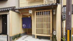 A traditional Japanese building with a wooden gate, a small entrance with a blue curtain, and a tiled roof. - Rinn Miyagawacho Tsubaki (Kyoto)