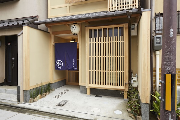 A traditional Japanese building with a wooden gate, a small entrance with a blue curtain, and a tiled roof.