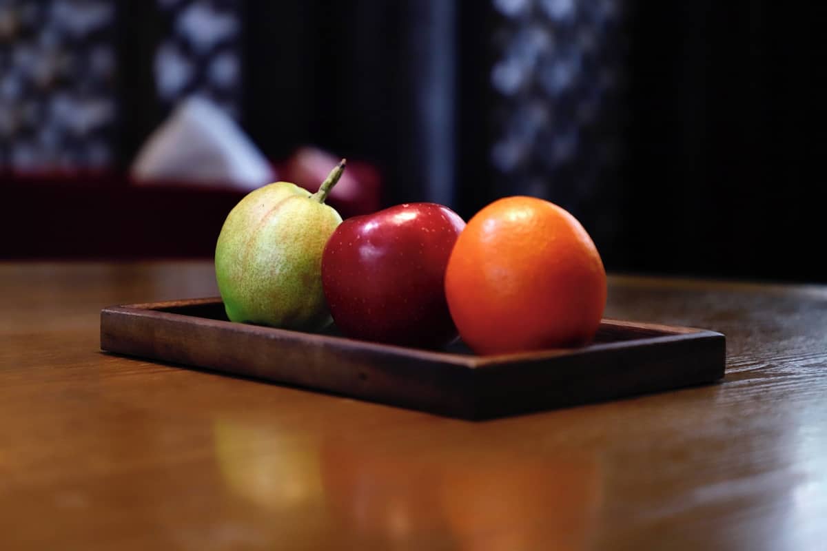 A wooden tray with a pear, an apple, and a tomato on a wooden table.