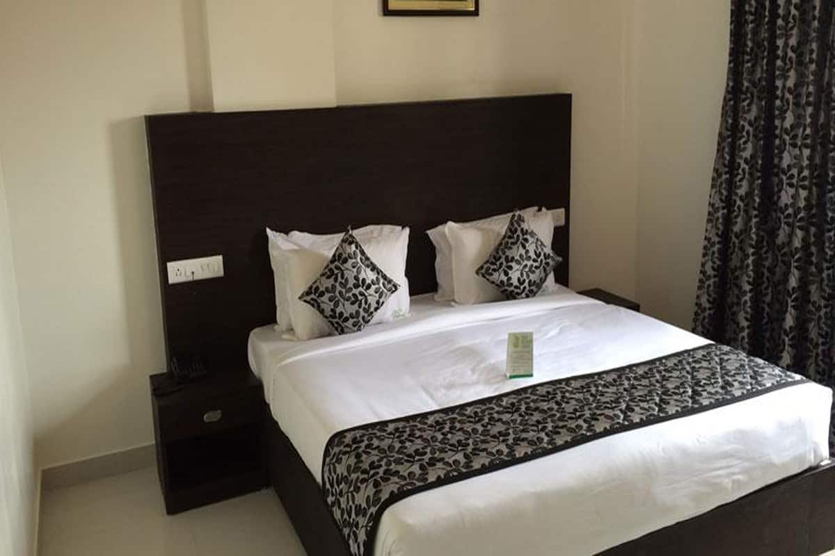 A neatly made bed with a dark headboard, white bedding, and two patterned pillows.