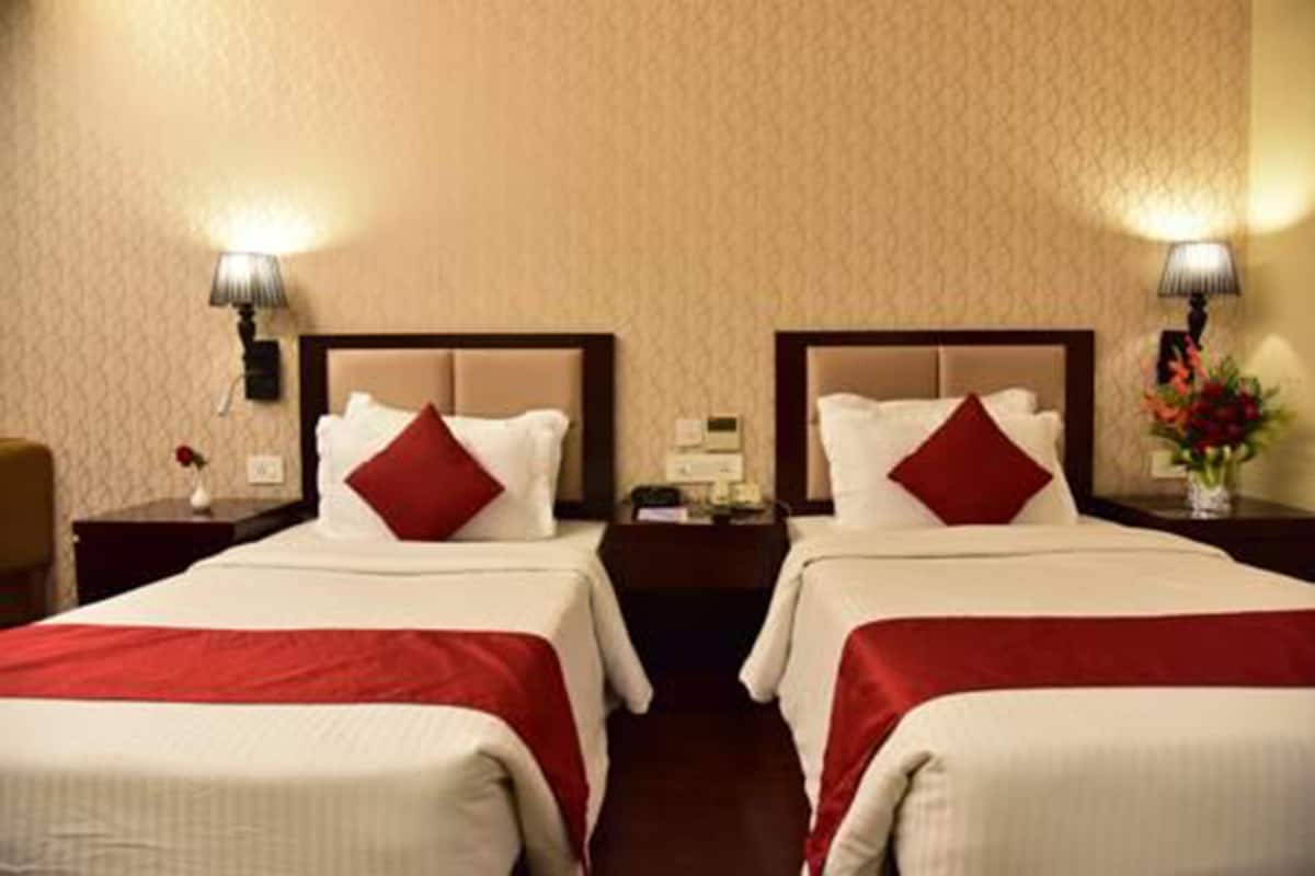 A hotel room with two beds, each with red bedding and white pillows, a nightstand with a lamp, and a vase with flowers on the right side.