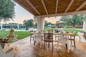 En udendørs terrasse med swimmingpool, overdækket siddeplads og et spisebord.