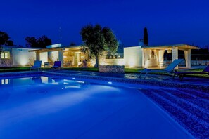 Et moderne hotel med swimmingpool, udendørs siddepladser og en godt oplyst terrasse.