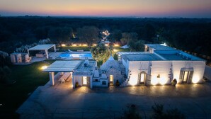 A large estate with multiple buildings, a swimming pool, and a well-lit outdoor area at dusk.