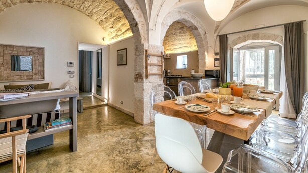 A spacious dining area with a wooden table set for breakfast, clear chairs, and a view of the kitchen in the background.