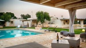 A poolside area with lounge chairs, a table with a bottle and glass, and a covered patio.