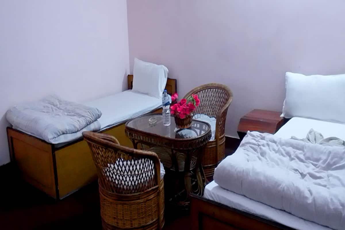 A small, neatly arranged room with a single bed, a chair, a small table, and a nightstand.