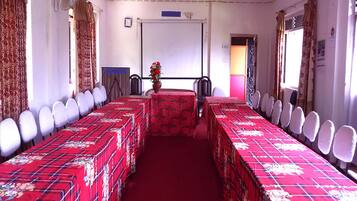 A conference room with long tables, white chairs, a projector screen, and a floral centerpiece.