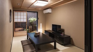 A modern living room with a wooden ceiling, a sliding glass door leading to a garden, a flat-screen TV, and a dark-colored sofa. - Rinn Manjuji (Kyoto)