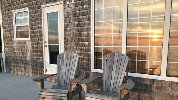 A wooden deck with two Adirondack chairs and a white door. - Cliff Waters Cottage, Private oceanfront secluded relaxation, Pleasant Bay, NS (Pleasant Bay)