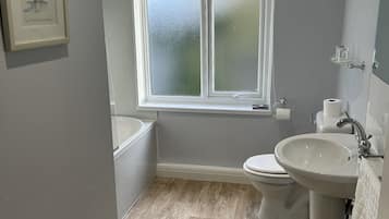 A bathroom with a bathtub, toilet, and sink, featuring a wooden floor and a frosted window.