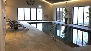 A modern indoor pool area with a clear view of the sky through large windows, a clock on the wall, and a fire extinguisher mounted on the wall. - Burton Lodge Guest House and Spa (Driffield)