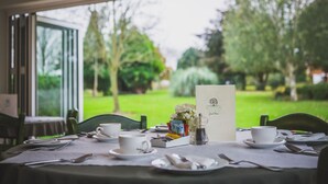 A dining table set with white tableware, a menu, and a vase of flowers. - Burton Lodge Guest House and Spa (Driffield)