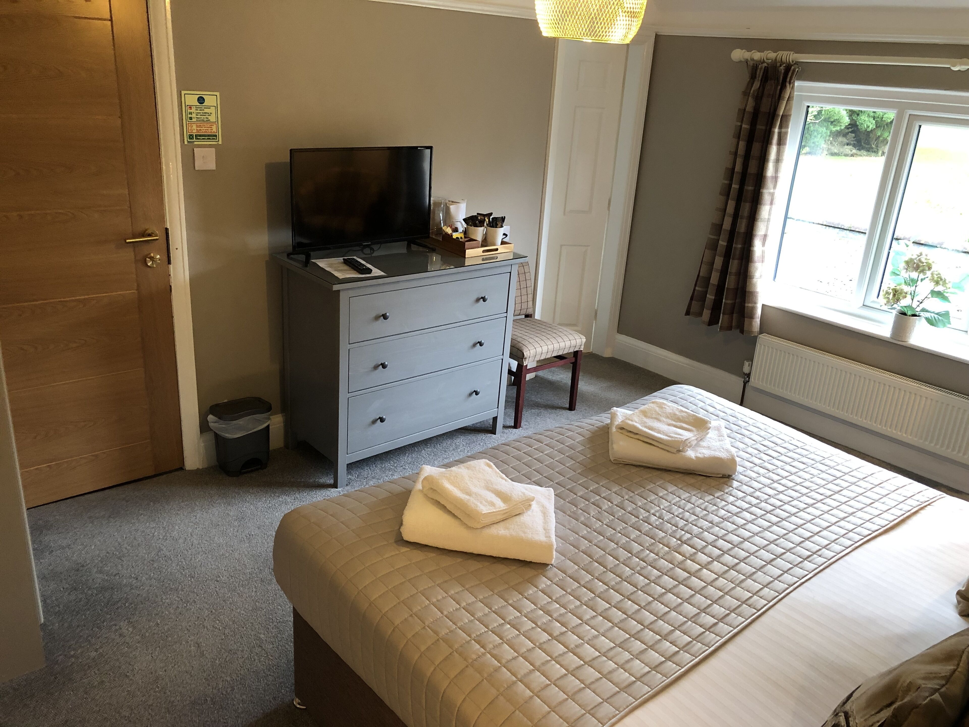 A hotel room with a bed, a desk with a television, a chair, and a window with curtains.