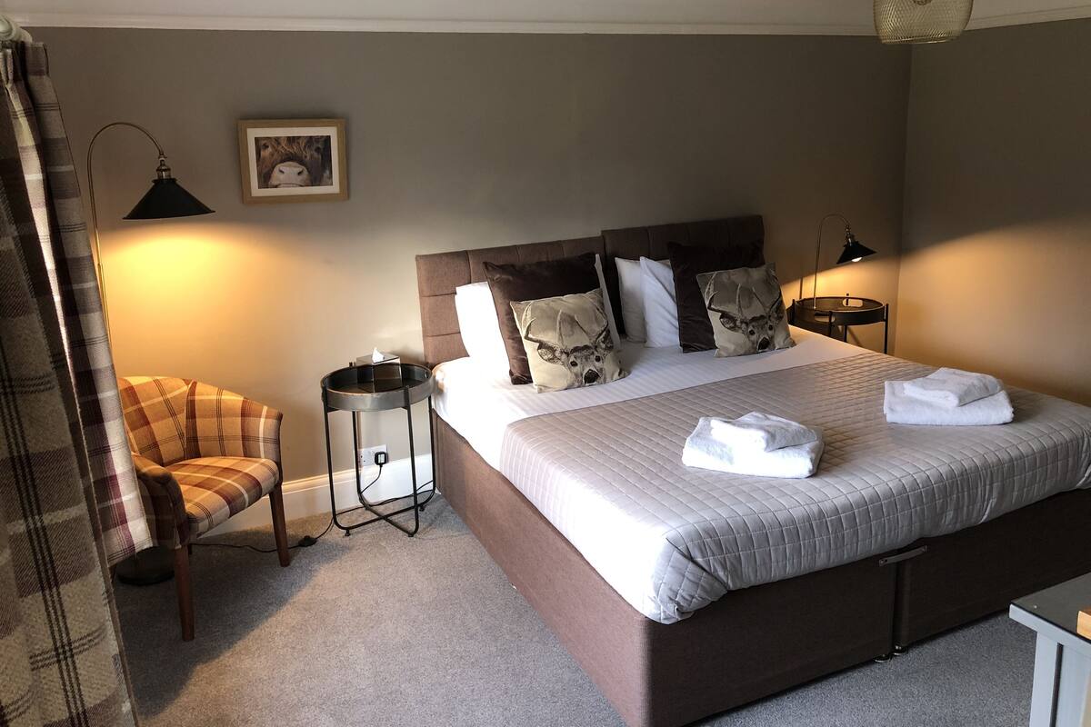 A neatly arranged bedroom with a large bed, two bedside tables, a chair, and a lamp.