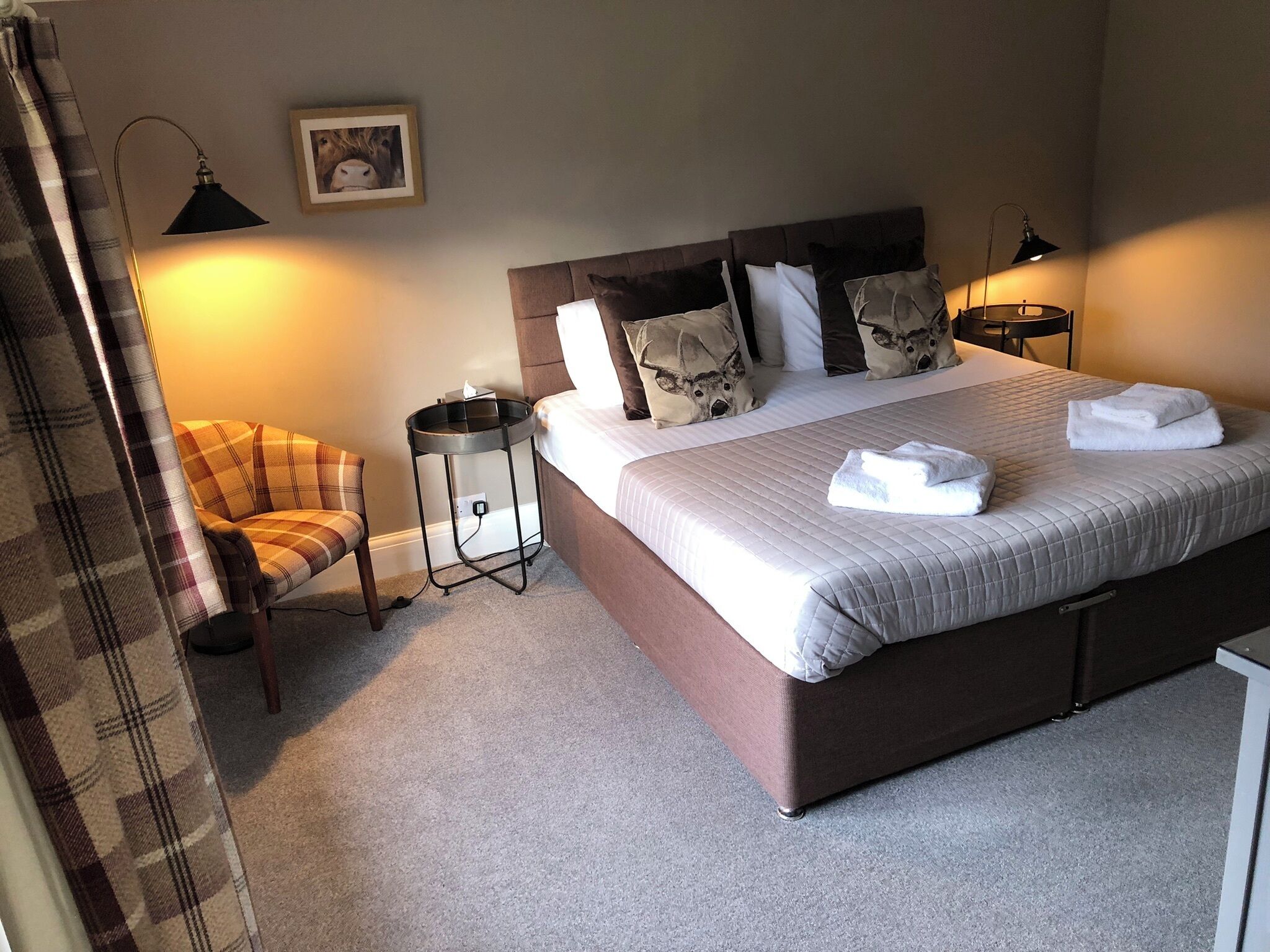 Een keurig opgemaakt slaapkamer met een groot bed, een stoel, een nachtkastje en een lamp.