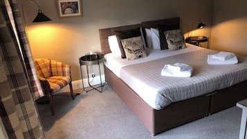 Een keurig opgemaakt slaapkamer met een groot bed, een stoel, een nachtkastje en een lamp.