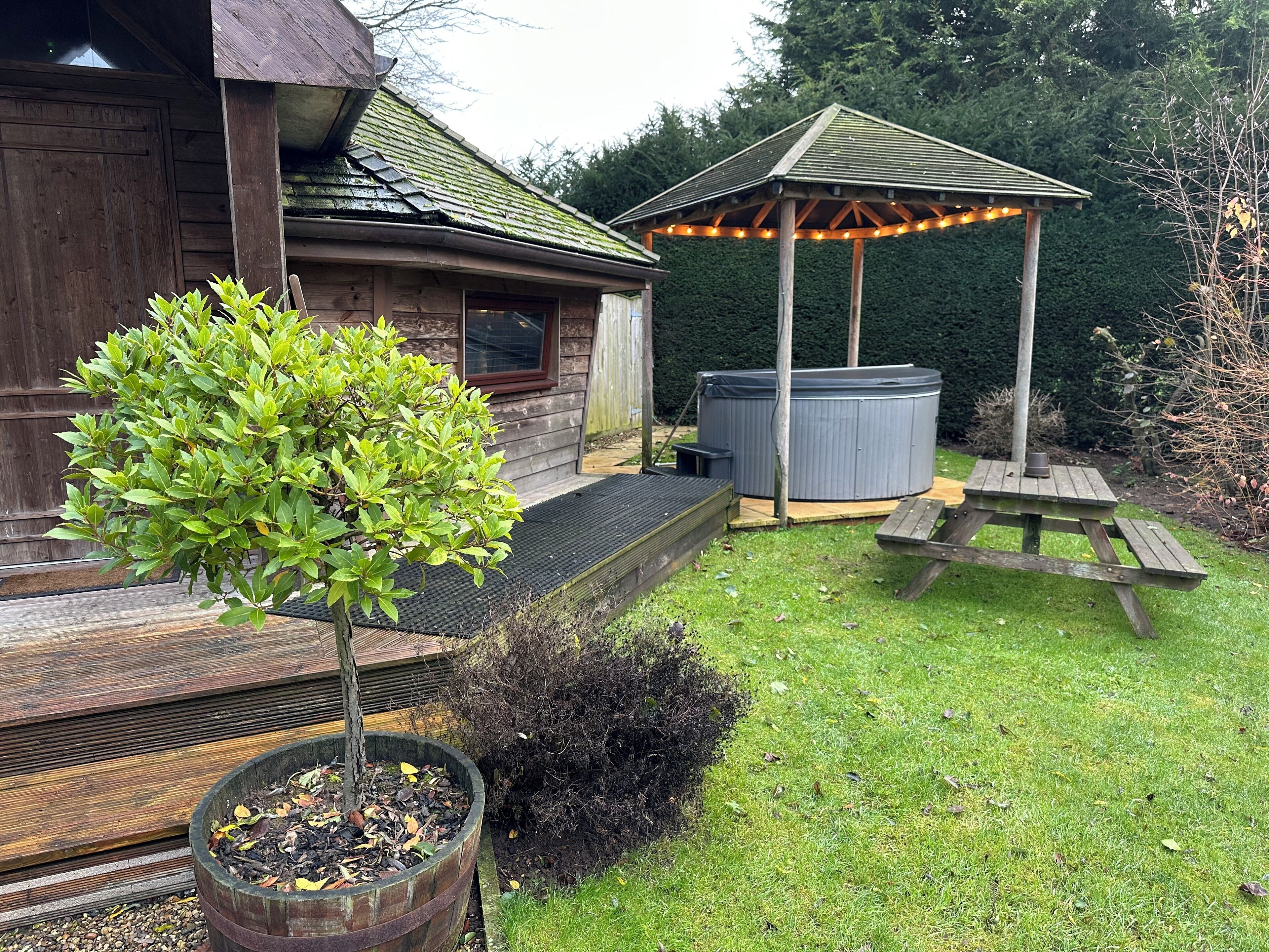 A wooden house with a covered patio, a hot tub, and a gazebo with string lights.