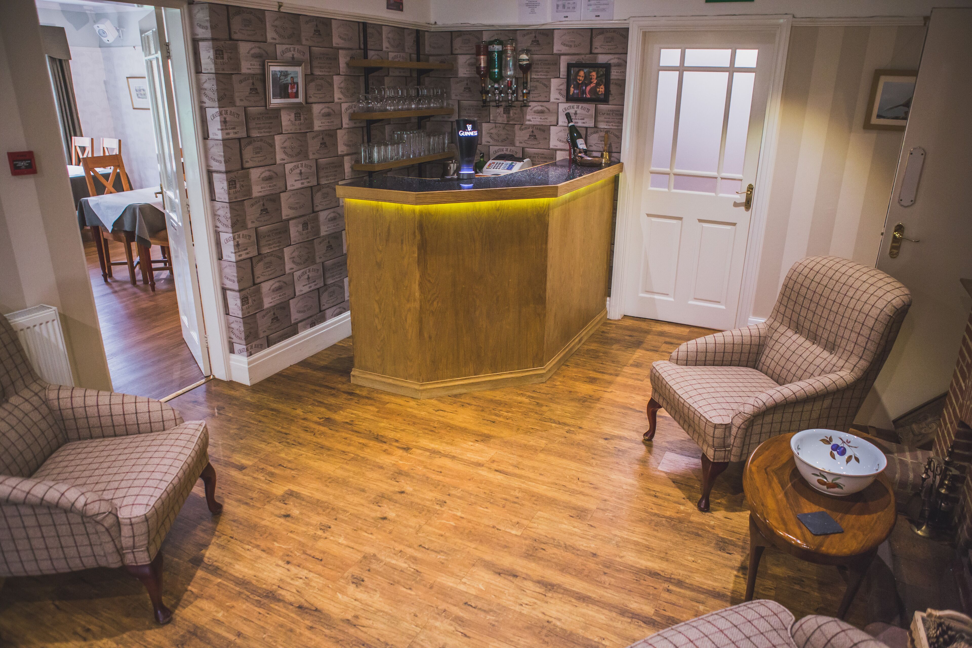 Una zona de bar con mostrador de madera, un área de estar con dos sillones y una mesa de comedor con sillas.