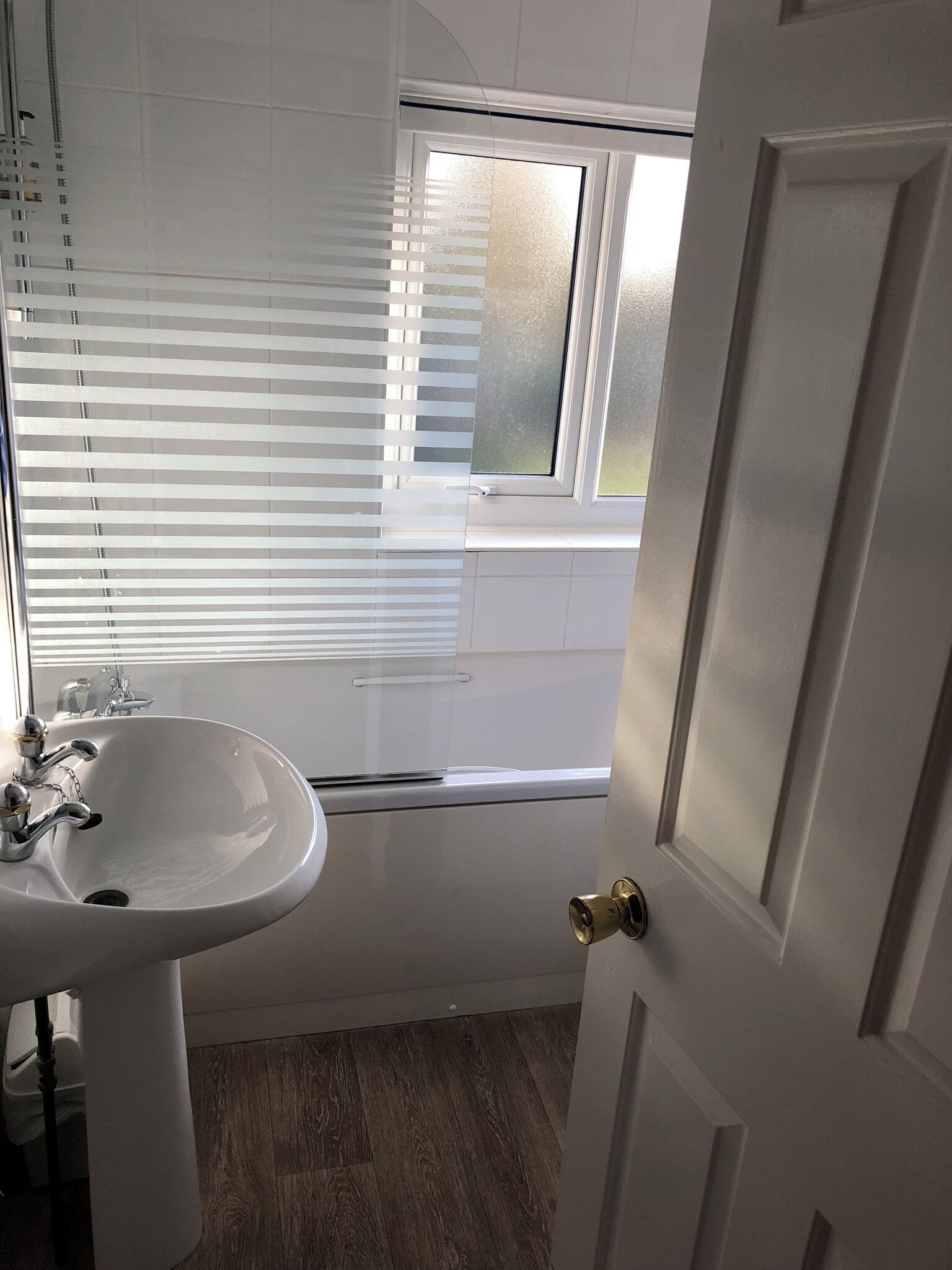 Un baño con lavamanos blanco, una ventana con persianas y una puerta.