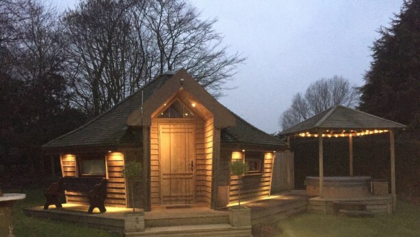 A log cabin with a wooden door, a porch, and a covered outdoor seating area with string lights. - Burton Lodge Guest House and Spa (Driffield)