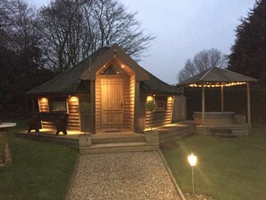 A log cabin with a wooden door, a porch, and a covered outdoor seating area with string lights. - Burton Lodge Guest House and Spa (Driffield)