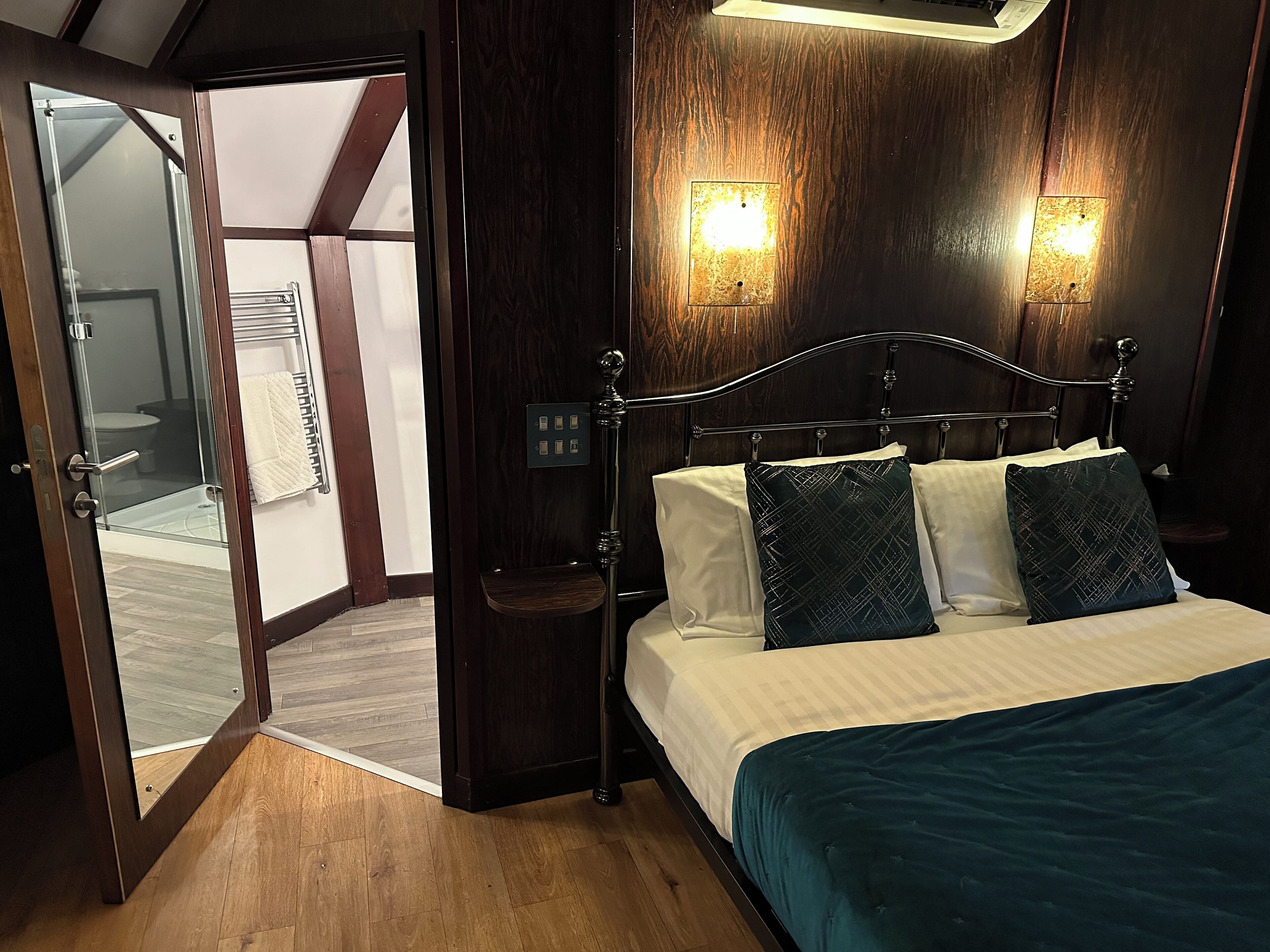 A bedroom with a wooden headboard, two bedside lamps, a bed with white linens and teal bedding, and a wooden floor.