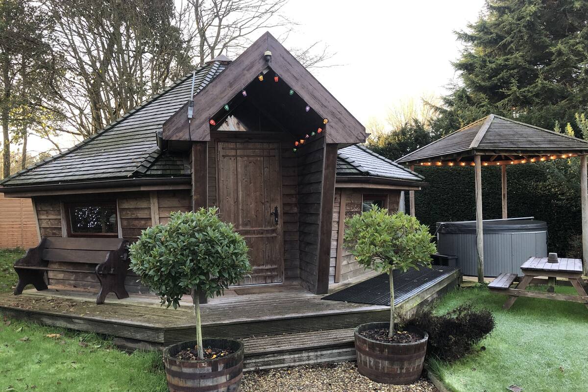 A rustic wooden cabin with a sloped roof, a wooden porch, and a small garden area with potted plants.