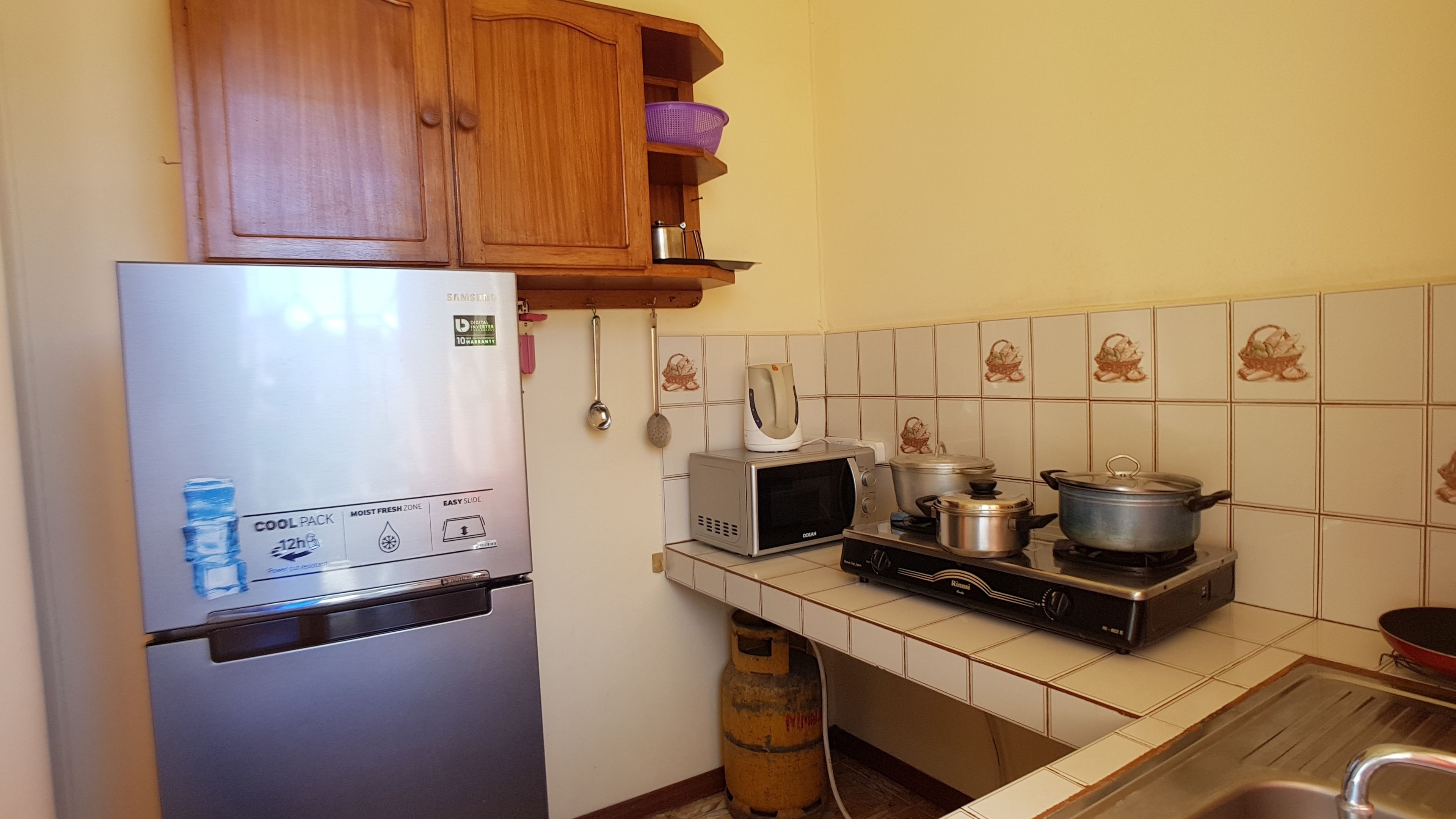 Cozinha equipada com geladeira, micro-ondas, fogão e painel de azulejos.