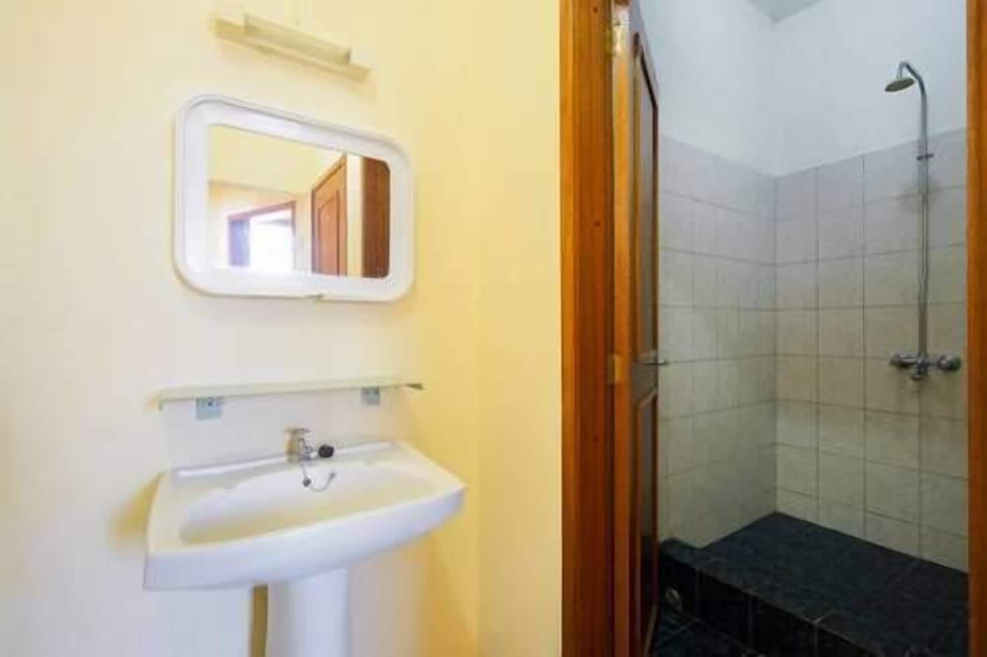 Un baño con lavamanos blanco, un espejo y zona de ducha.