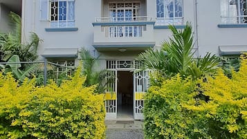 A multi-story building with balconies, a gravel pathway, and yellow flowering bushes.