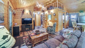 Interior de una cabaña de madera con sala de estar, comedor y un dormitorio en el altiloque.