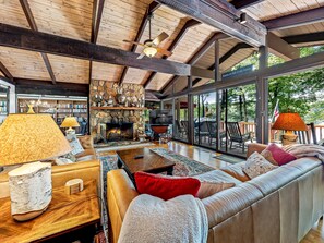 A spacious living room with a stone fireplace, leather sofa, and large windows overlooking a lake.