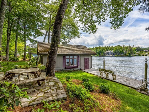 A lakeside cabin with a dock, surrounded by lush greenery and a view of the lake.