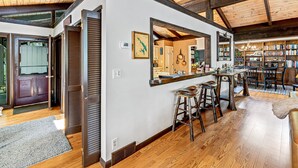 Una cocina amplia con vigas de madera, una zona de bar con taburetes y una estantería grande llena de libros.