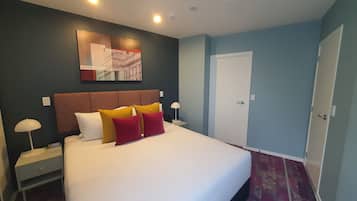 A hotel room with a large bed, a headboard, a nightstand, a lamp, a door, and a wall-mounted artwork.