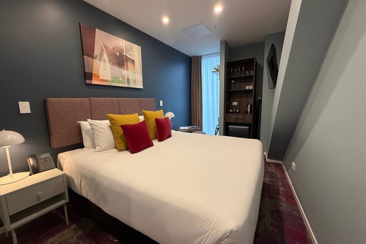 A hotel room with a large bed, bedside table with a lamp, a telephone, and a painting on the wall.