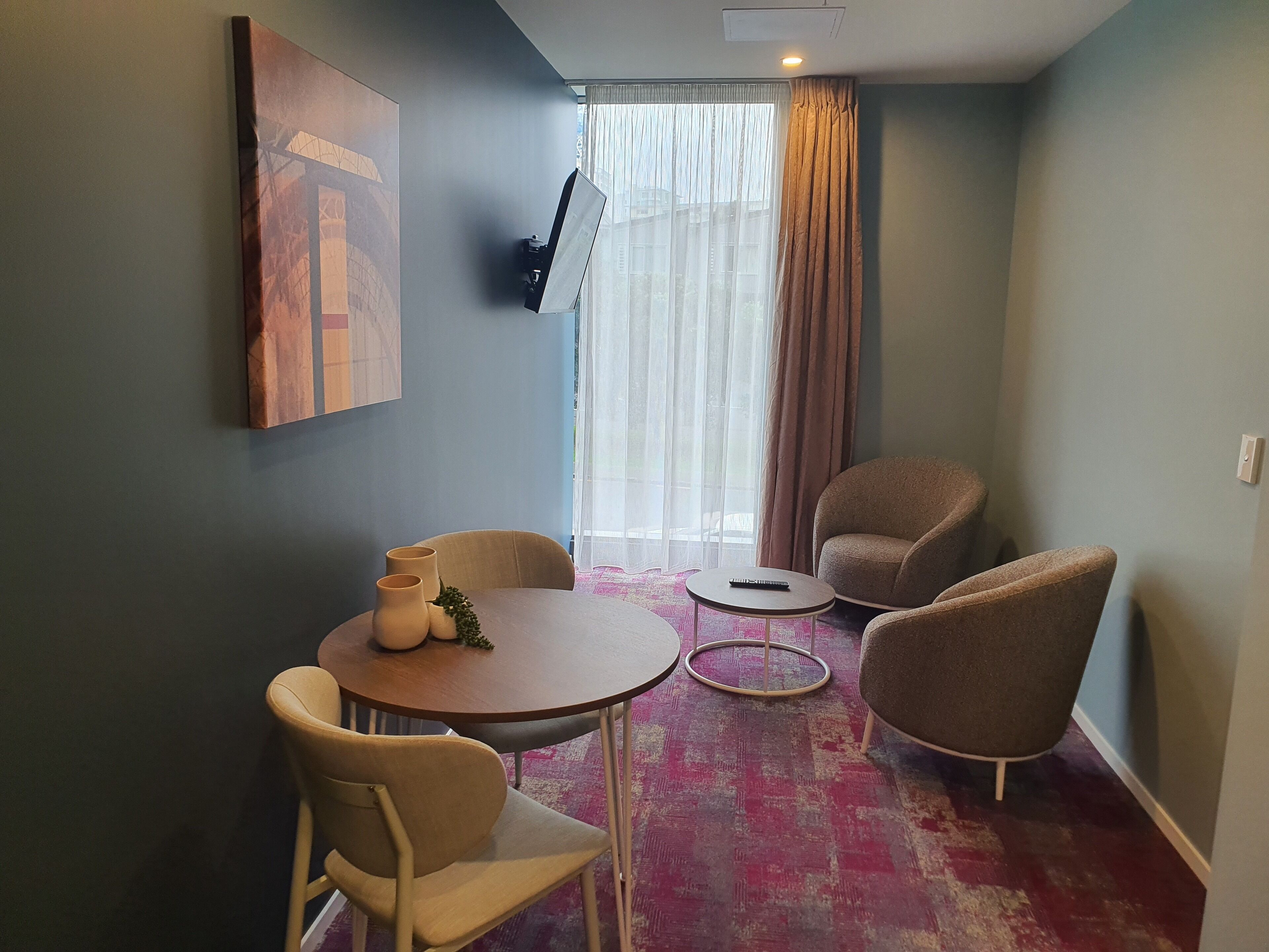 A modern room with a round dining table, two chairs, a small side table, and a sofa.
