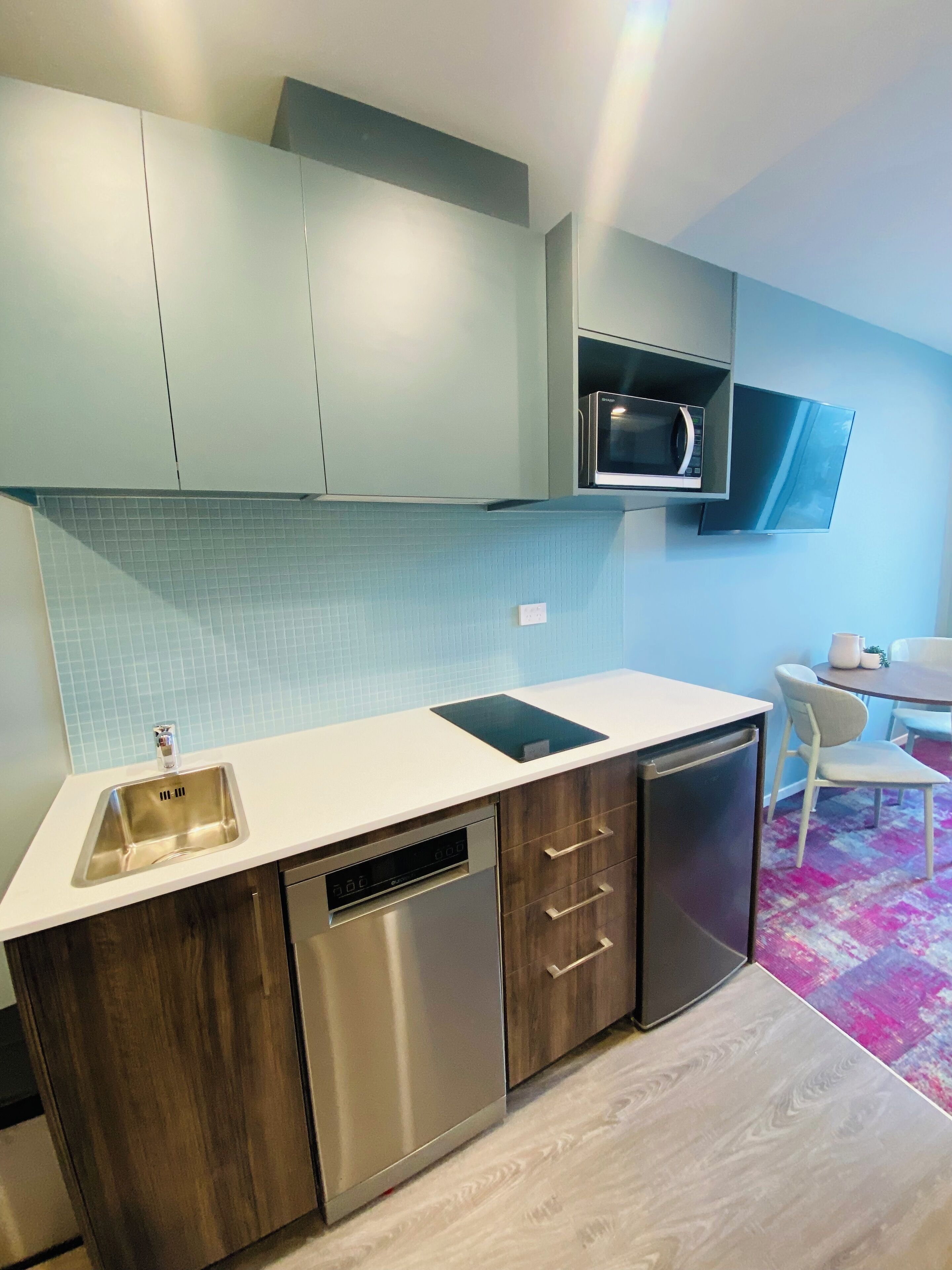 A modern kitchen with a dishwasher, microwave, and a built-in oven. There is a dining area with a table and chairs.