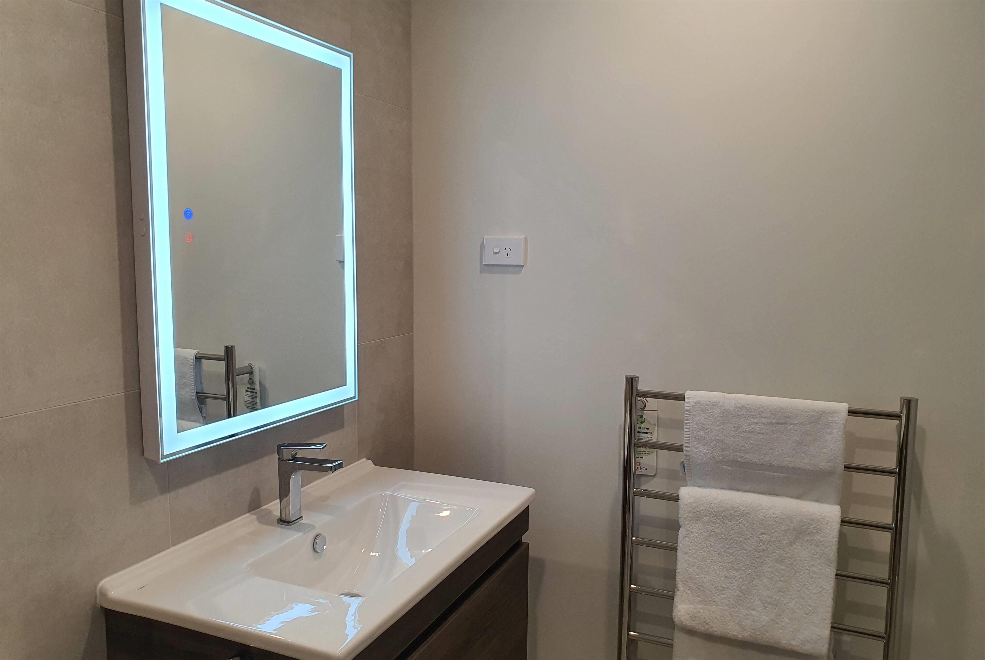 A bathroom with a white sink, a mirror with a light, and a towel rack with two towels.