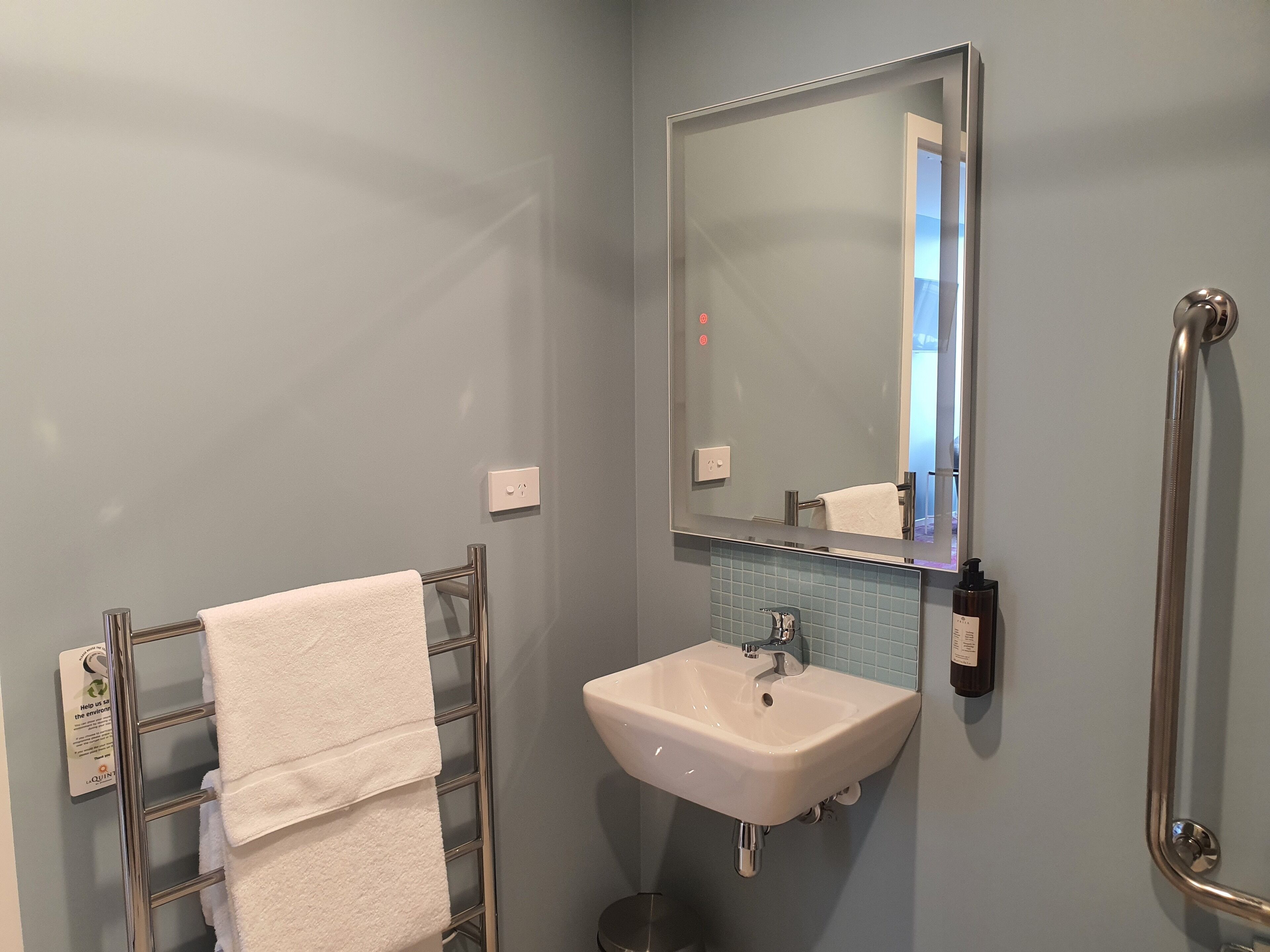 A bathroom with a white sink, a mirror, and a towel rack with a white towel.