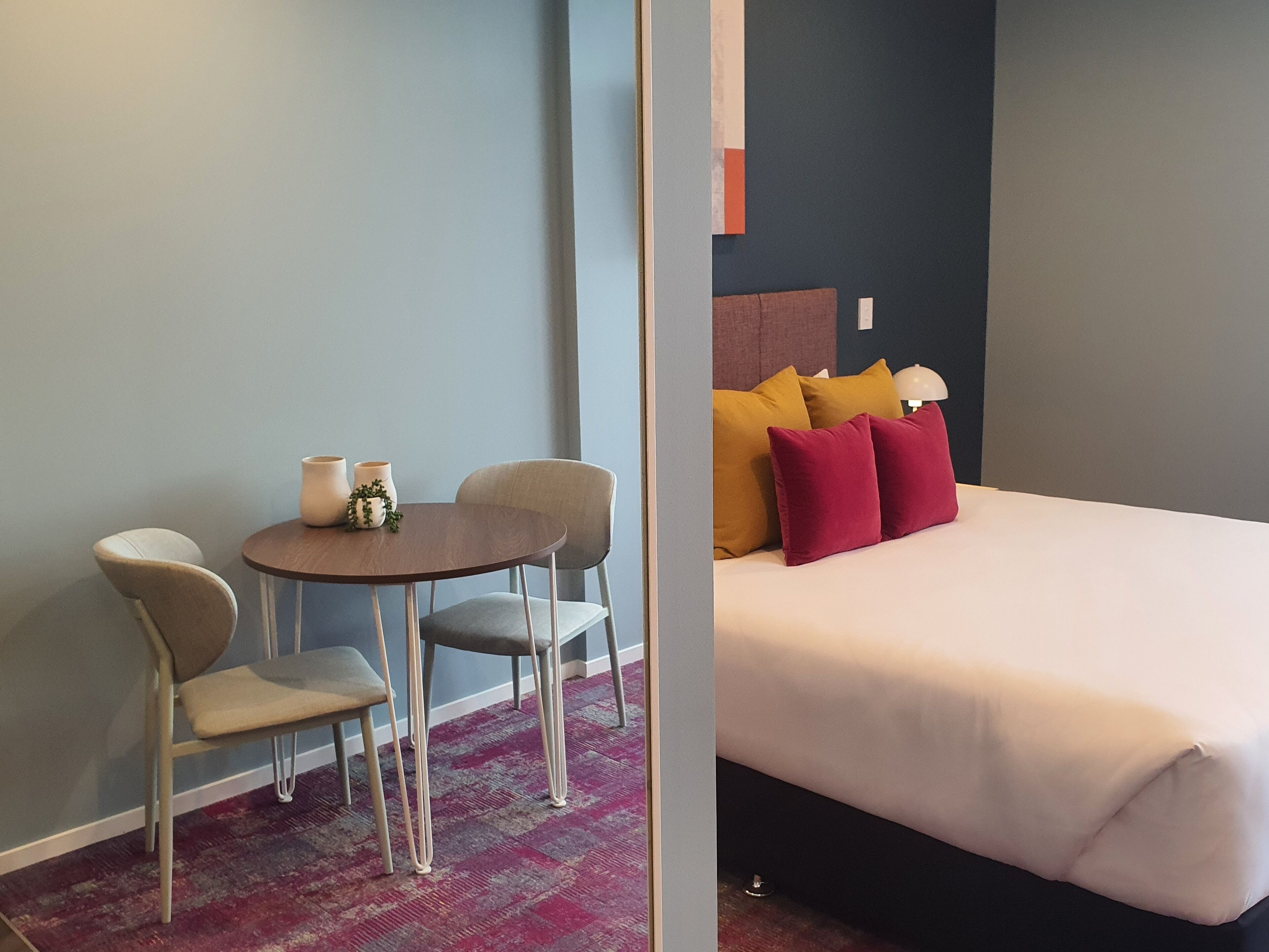 Una habitación de hotel con una cama, una mesita redonda con sillas y una planta decorativa.