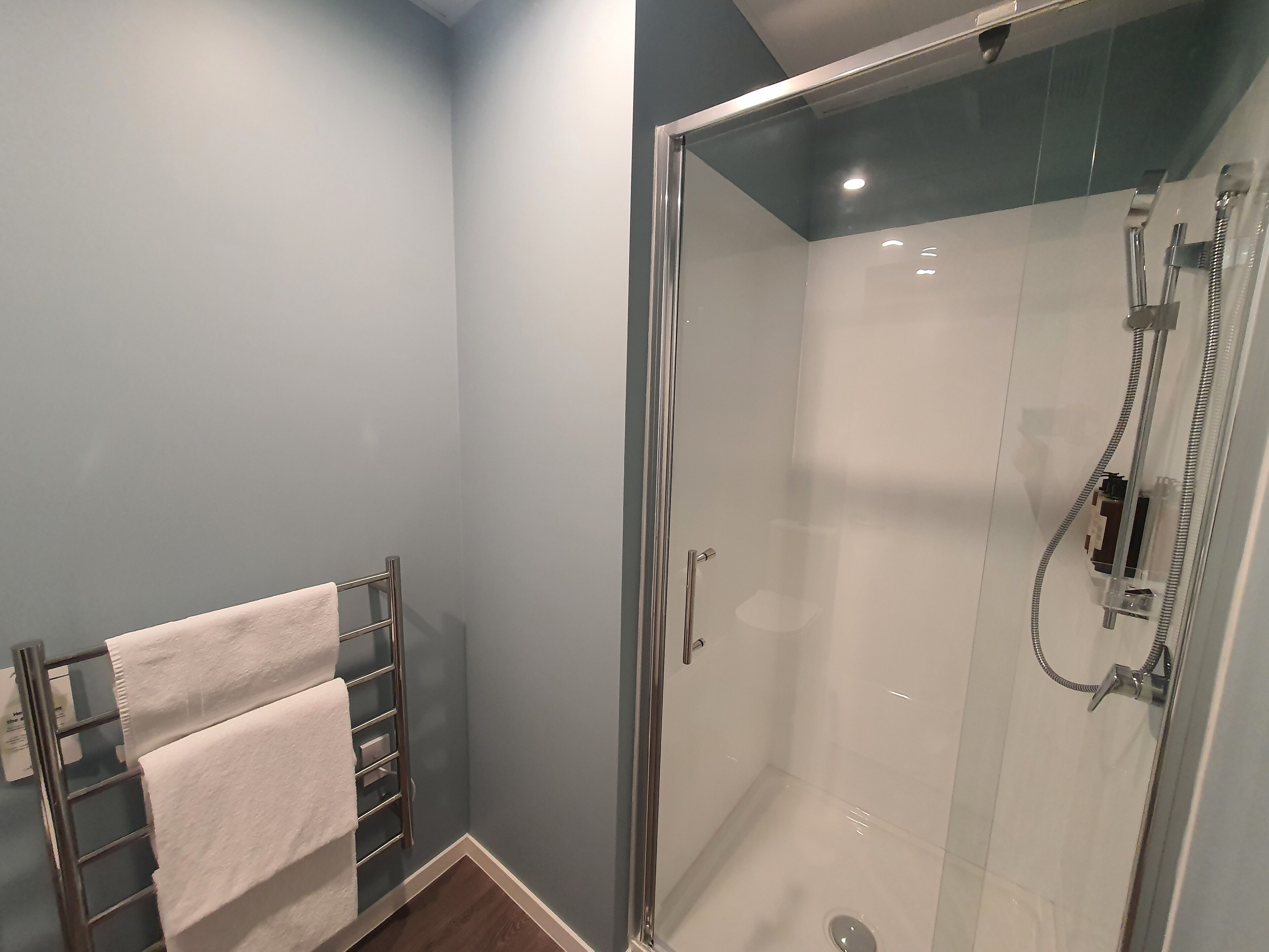 Une douche fermée par des parois en verre, dotée d’un pommeau de douche à main et d’un robinet à main.