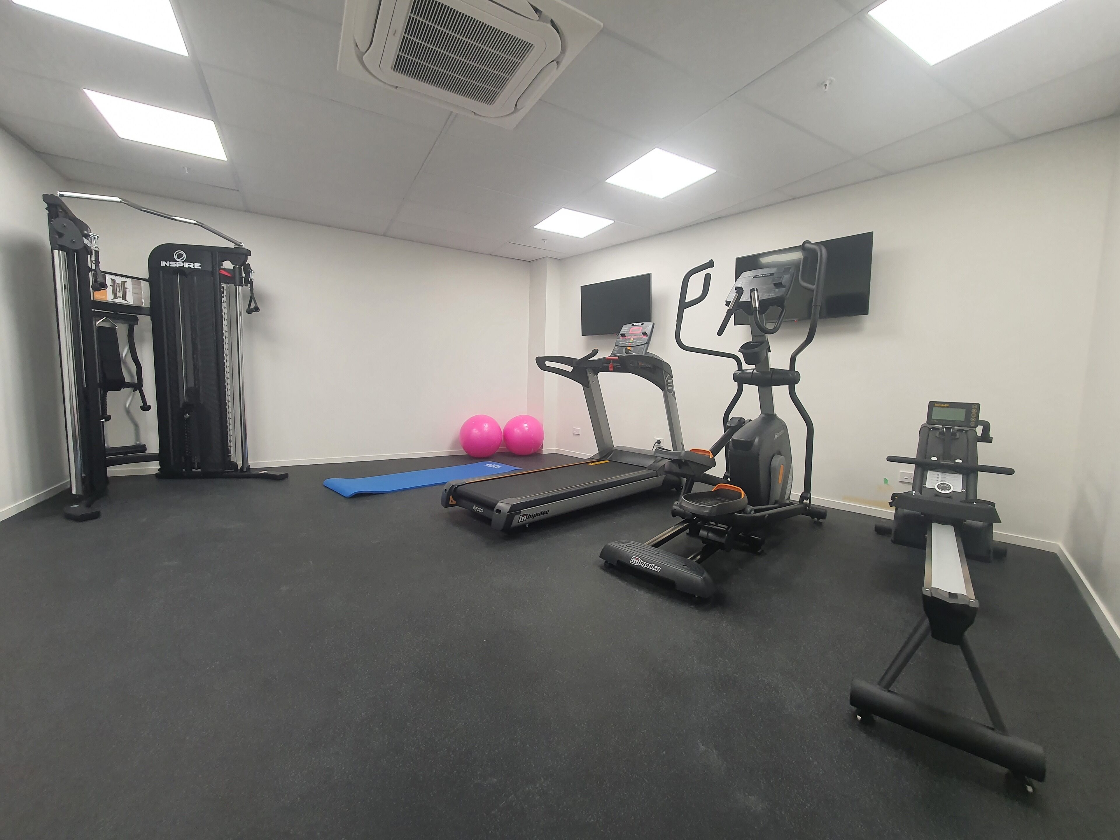 A gym with treadmills, elliptical machines, a weight bench, and exercise balls.