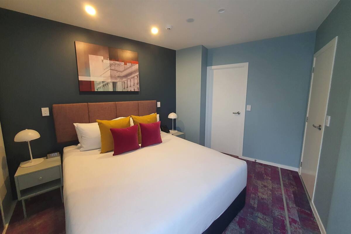 A hotel room with a large bed, a nightstand, a wall-mounted artwork, and a door.