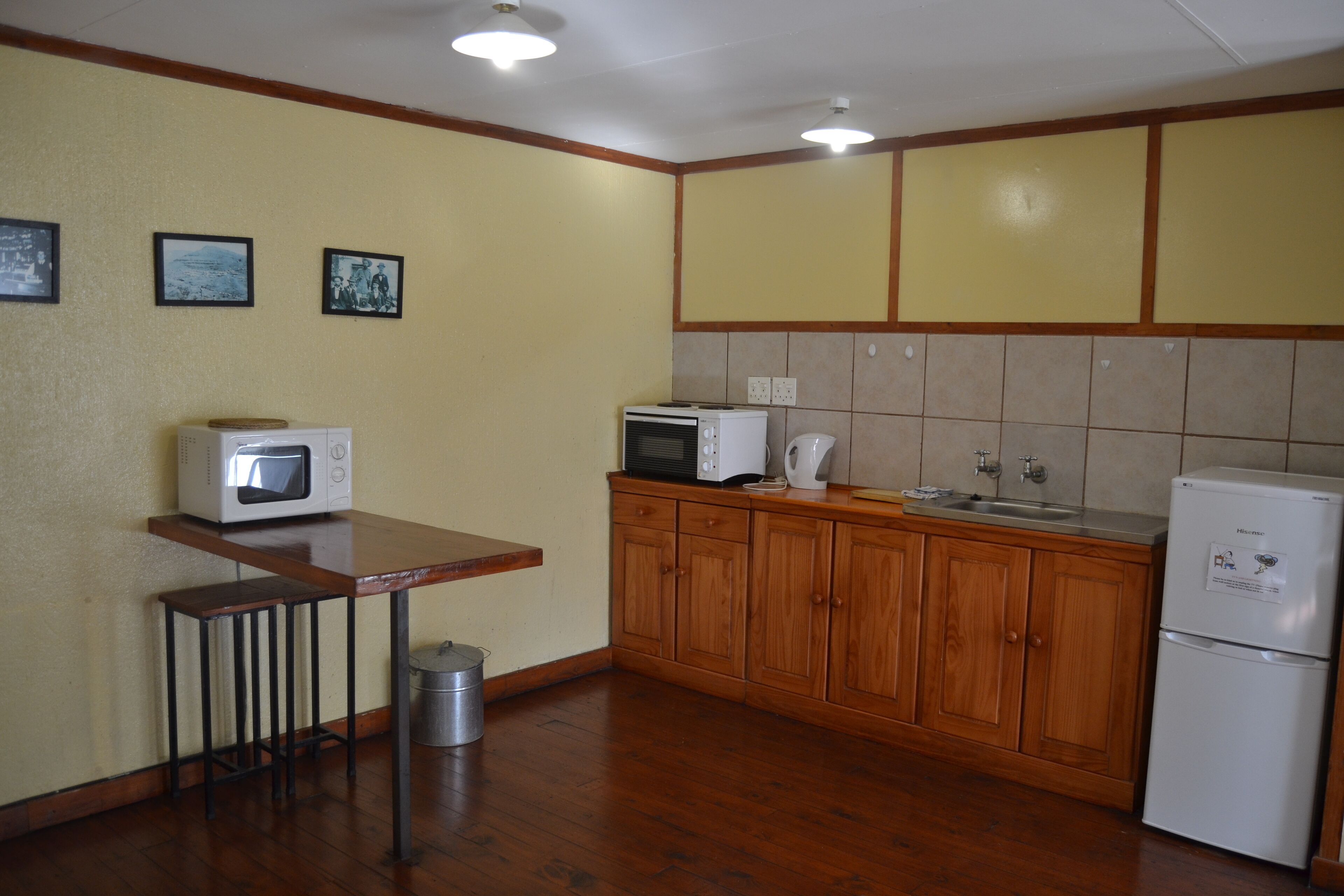 A compact kitchen with wooden cabinets, a microwave, a toaster, and a refrigerator.