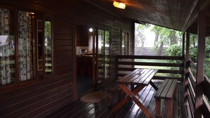 A wooden cabin with a porch, a dining area, and a kitchen visible through an open door. - Log Cabin & Settlers Village (Graskop)