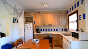 A compact kitchen with wooden cabinets, a dining table with chairs, a microwave, and a coffee maker. - PIVERD DEL GOLF 74 (Pals)