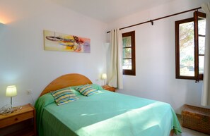 A bedroom with a bed, a nightstand, a lamp, a painting, a window, and a curtain rod.